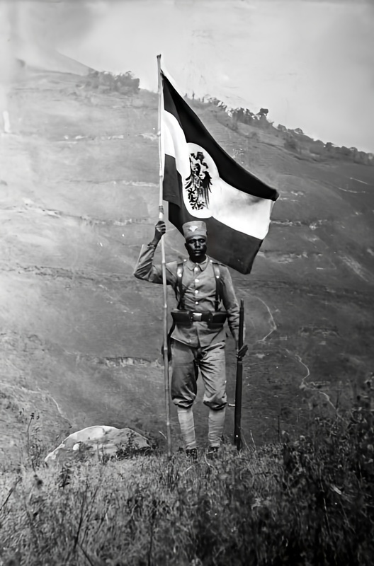 An African Askari soldier in German East Africa with the flag of the German Empire